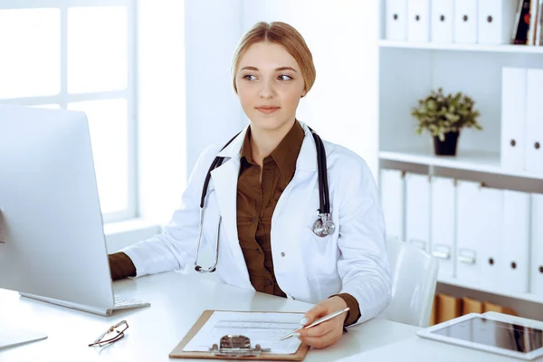 Mujer joven médico en el trabajo en el hospital mirando monitor de escritorio PC. El médico controla los registros de la historia de la medicación y los resultados del examen. Concepto de medicina y salud — Foto de Stock