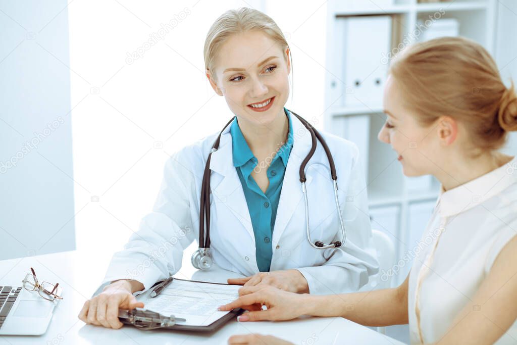 Doctor and patient talking in hospital office while sitting at the desk. Health care and client service in medicine