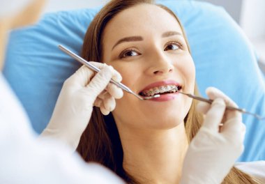 Diş hekiminde dişçi tarafından incelenen diş telleriyle gülümseyen genç bir kadın. Sağlıklı diş ve ilaç konsepti