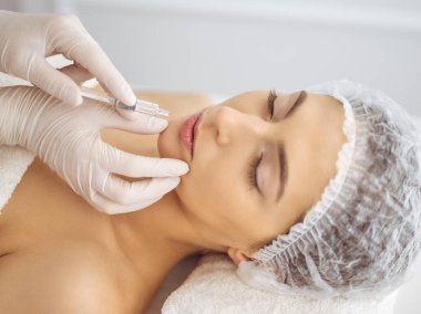 Güzellik uzmanı, genç esmer kadının yüzüne şırıngayla güzellik prosedürü uyguluyor. Kozmetik ilaç ve ameliyat, güzellik iğneleri.