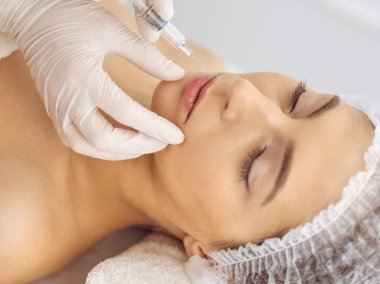 Güzellik uzmanı, genç esmer kadının yüzüne şırıngayla güzellik prosedürü uyguluyor. Kozmetik ilaç ve ameliyat, güzellik iğneleri.