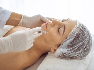 Güzellik uzmanı, genç esmer kadının yüzüne şırıngayla güzellik prosedürü uyguluyor. Kozmetik ilaç ve ameliyat, güzellik iğneleri.