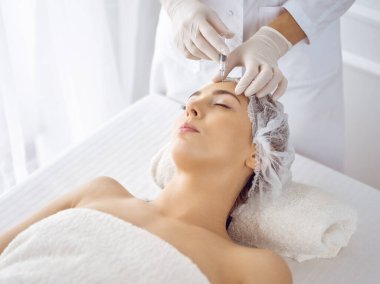 Güzellik uzmanı, genç esmer kadının yüzüne şırıngayla güzellik prosedürü uyguluyor. Kozmetik ilaç ve ameliyat, güzellik iğneleri.