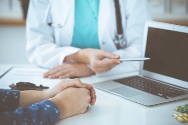 Doktor dizüstü bilgisayarı işaret ederken bir doktor ve hastanın masadaki yakın çekimleri. İlaç ve sağlık hizmetleri kavramı