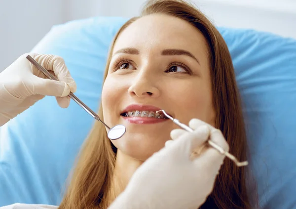 Diş hekiminde dişçi tarafından incelenen diş telleriyle gülümseyen genç bir kadın. Sağlıklı diş ve ilaç konsepti — Stok fotoğraf