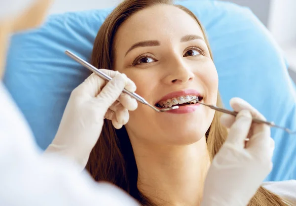 Glimlachende jonge vrouw met orthodontische haakjes onderzocht door tandarts in tandheelkundige kliniek. Gezonde tanden en geneeskundeconcept — Stockfoto