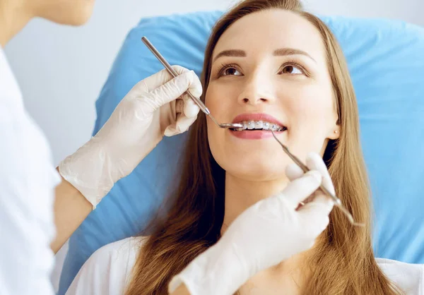 Glimlachende jonge vrouw met orthodontische haakjes onderzocht door tandarts in tandheelkundige kliniek. Gezonde tanden en geneeskundeconcept — Stockfoto