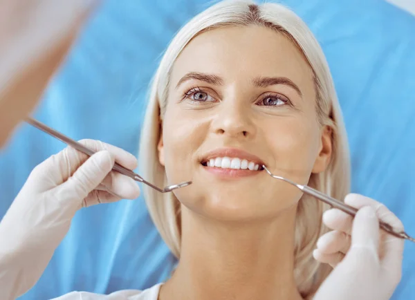 Lachende blonde vrouw onderzocht door tandarts in de tandheelkundige kliniek. Gezonde tanden en geneeskundeconcept — Stockfoto