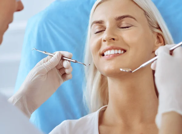 Lachende blonde vrouw onderzocht door tandarts in de tandheelkundige kliniek. Gezonde tanden en geneeskundeconcept — Stockfoto
