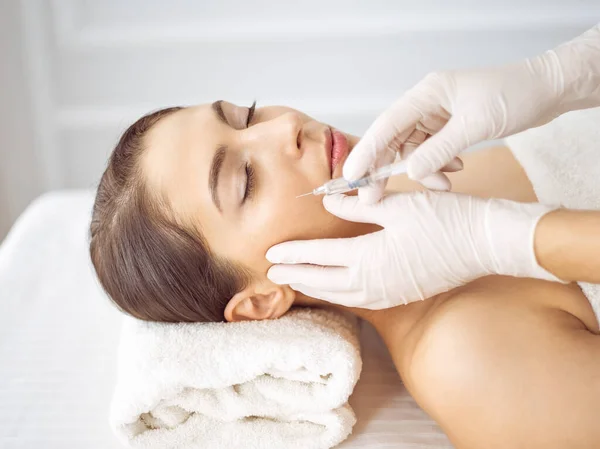 Schoonheidsspecialiste doet schoonheidsbehandeling met spuit tot aangezicht van jonge brunette vrouw. Cosmetische geneeskunde en chirurgie, schoonheidsinjecties — Stockfoto