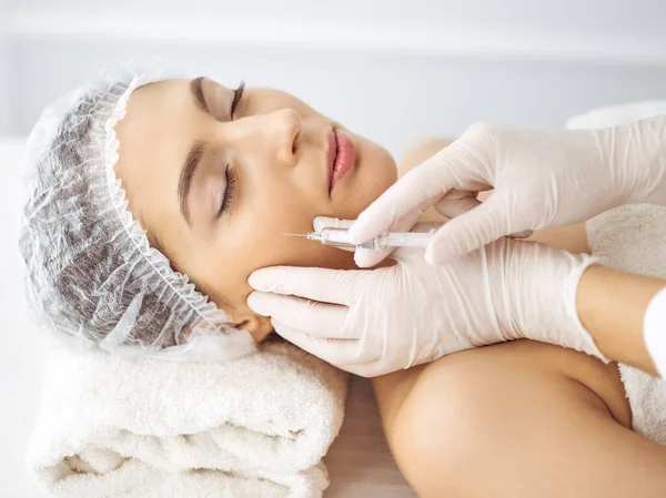 Beautician doing beauty procedure with syringe to face of young brunette woman. Cosmetic medicine and surgery, beauty injections