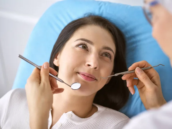 Lachende brunette vrouw wordt onderzocht door tandarts in de tandheelkundige kliniek. Handen van een arts met tandheelkundige instrumenten in de buurt van de mond van patiënten. Gezonde tanden en geneeskundeconcept — Stockfoto