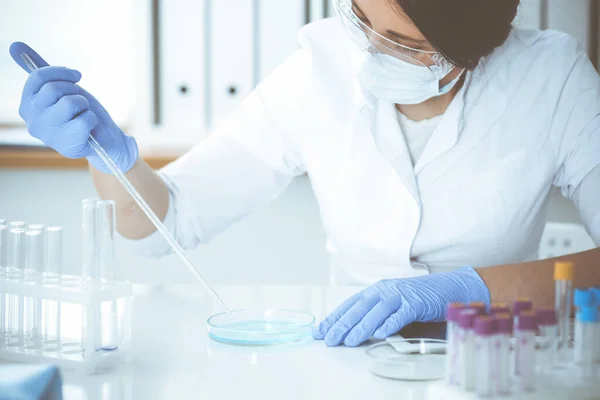 Koruyucu gözlüklü profesyonel kadın bilim adamının laboratuarda reaktörlerle deney yapması. Tıp ve araştırma konsepti