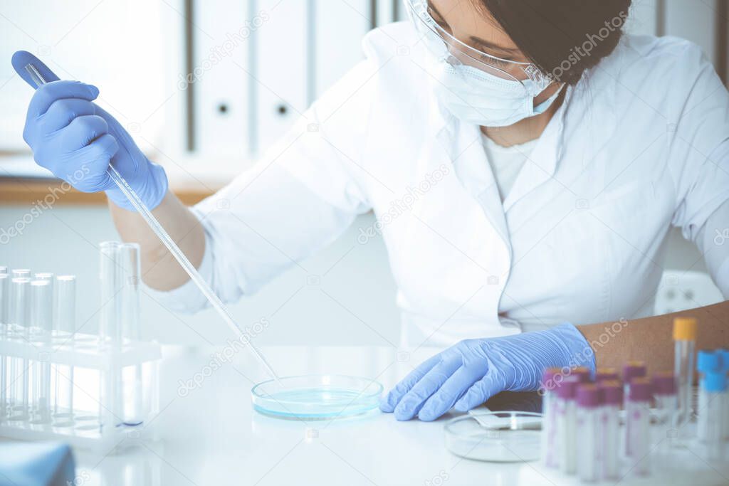 Close-up of professional female scientist in protective eyeglasses making experiment with reagents in laboratory. Medicine and research concept