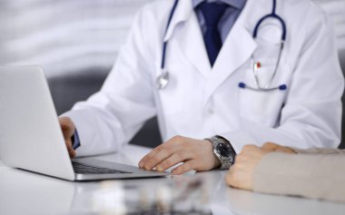 Bilinmeyen erkek doktor ve hasta kadın klinikte oturup dizüstü bilgisayar kullanırken bir şeyler tartışıyorlar. Hastanedeki en iyi sağlık hizmeti, ilaç, salgın durdurma.