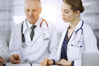 Doktorlar meslektaşları ve yaşlı terapist güneşli klinikte çalışırken güncel hastalık terapisini tartışıyorlar. Tıpta takım çalışması
