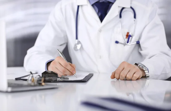 Médico desconhecido sentado e trabalhando com prancheta de registro de histórico de medicação na clínica em seu local de trabalho, close-up. Médico jovem no trabalho. Serviço médico perfeito, conceito de medicina — Fotografia de Stock