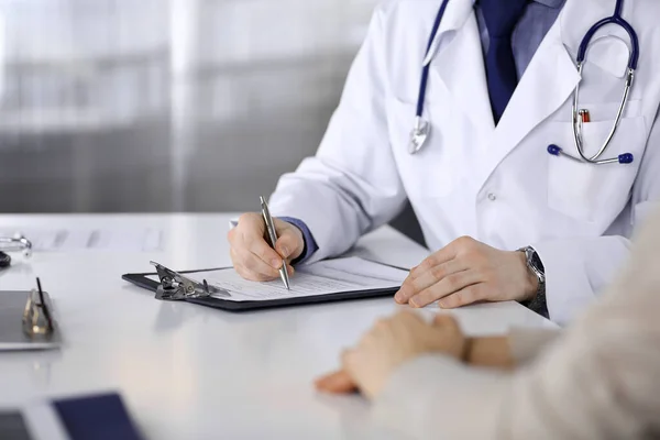 Unknown male doctor and patient woman discussing something while sitting in clinic and using clipboard. Best medical service in hospital, medicine, pandemic stop — Stock Photo, Image