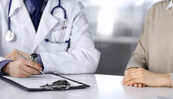 Unknown male doctor and patient woman discussing something while sitting in clinic and using clipboard. Best medical service in hospital, medicine, pandemic stop — Stock Photo, Image