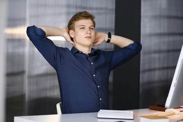 Young blond businessman and programmer stretching hands after working hard with computer. Startup business leads to success
