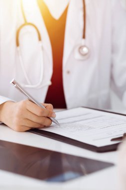Bilinmeyen kadın-doktor hastaya danışmanlık yaparken başvuru formu dolduruyor. güneşli oda tıp konseptinde