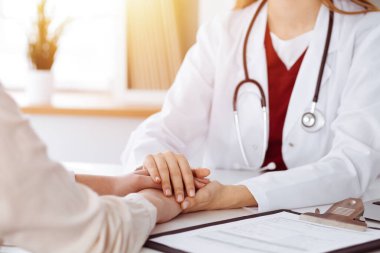 Kimliği belirsiz kadın doktorun elleri güneşli odada kadın hastasına güvence veriyor.