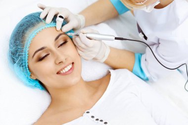 Kadın yüzüne kaş dövmesi yapan profesyonel bir güzellik uzmanı. Güzellik salonunda kalıcı kaş makyajı, yakın çekim. Kozmetoloji tedavisi