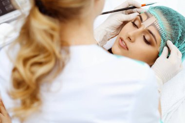 Profesyonel güzellik uzmanı kozmetik cetvel kullanarak kaş çizgisini düzeltecek. Güzellik salonunda kalıcı kaş makyajı, yakın çekim. Kozmetoloji tedavisi