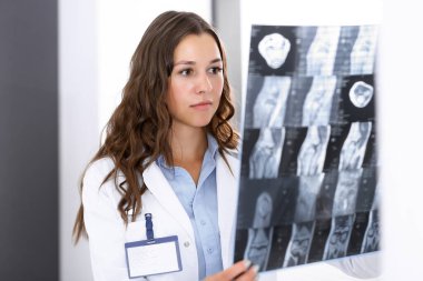 Doktor kadın hastanenin penceresinin yanında dikilirken röntgen filmini inceliyor. Cerrah ya da ortopedist. Tıp ve sağlık hizmetleri kavramı