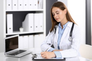 Hastane ofisindeki masada otururken doktor kadın form dolduruyor. Hekim iş başında. İlaç ve sağlık hizmetleri kavramı