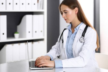 Doktor kadın hastane ofisindeki masada otururken dizüstü bilgisayarda yazıyor. Hekim iş başında. İlaç ve sağlık hizmetleri kavramı