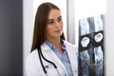 Doktor kadın hastanenin penceresinin yanında dikilirken röntgen filmini inceliyor. Cerrah ya da ortopedist. Tıp ve sağlık hizmetleri kavramı