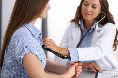 Elinde steteskop olan bir doktor kadın hastasını muayene ediyor. Sağlık, kardiyoloji ve tıp kavramları