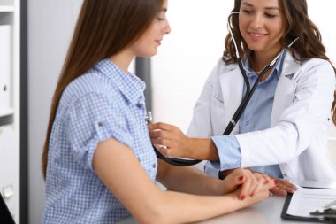 Elinde steteskop olan bir doktor kadın hastasını muayene ediyor. Sağlık, kardiyoloji ve tıp kavramları