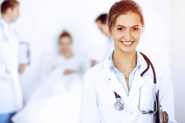 Doctora sonriendo en el fondo con paciente en la cama y dos doctores — Foto de Stock