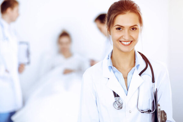 Female doctor smiling on the background with patient in the bed and two doctors