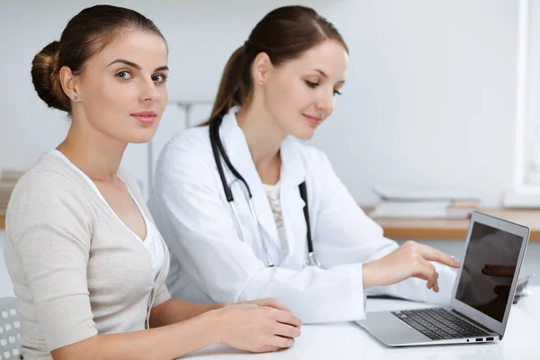 ノートパソコンを使用している間、医師と患者は健康診断結果を座って議論しています。医療、医療、良いニュースの概念 — ストック写真
