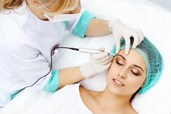 Esteticista profissional fazendo tatuagem de sobrancelha no rosto da mulher. Maquiagem permanente da testa no salão de beleza, close-up. Tratamento de cosmetologia — Fotografia de Stock