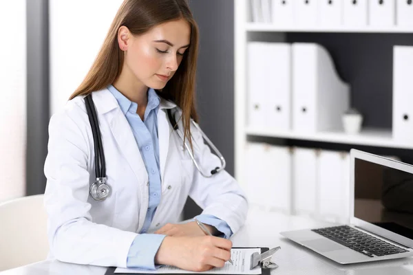 Mujer doctora llenando formulario médico mientras está sentada en el escritorio en la oficina del hospital. Médico trabajando. Concepto de medicina y salud — Foto de Stock