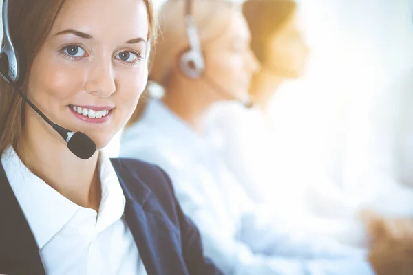 Cheerful smiling business woman with headphones consulting clients. Group of diverse phone operators at work in sunny office.Call center and business people concept — Stock Photo, Image