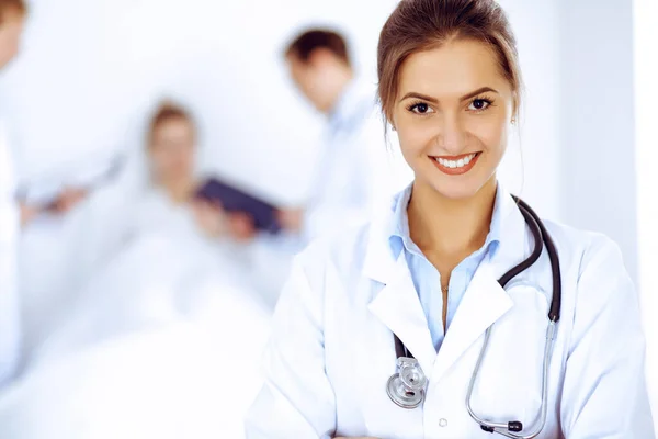 Doctora sonriendo en el fondo con paciente en la cama y dos doctores Imagen de stock