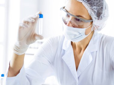 Koruyucu gözlüklü profesyonel kadın bilim adamı laboratuarda reaktörlerle araştırma tüpü kullanıyor. Tıp ve bilim araştırmaları kavramları