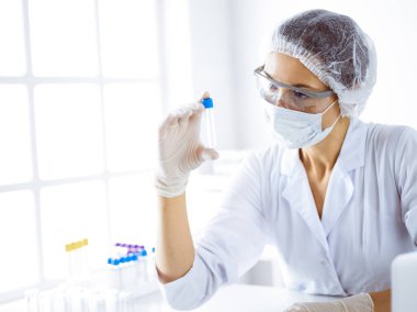 Koruyucu gözlüklü profesyonel kadın bilim adamı laboratuarda reaktörlerle araştırma tüpü kullanıyor. Tıp ve bilim araştırmaları kavramları