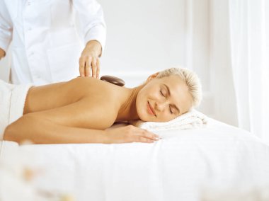 Güzel sarışın kadın sıcak taşlardan hoşlanıyor ve gözleri kapalı. Spa konsepti