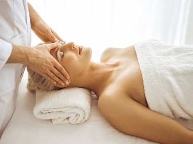 Güzel sarışın kadın kapalı gözlerle yüz masajından hoşlanıyor. Tıp ve kaplıca merkezi kavramlarında rahatlatıcı tedavi