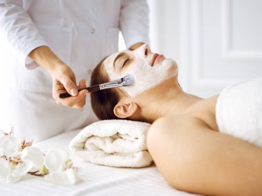 Güzel esmer kadın kapalı gözlerle kozmetik maske takmaktan zevk alıyor. Tıp ve kaplıca merkezi kavramlarında rahatlatıcı tedavi