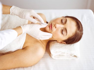 Güzellik uzmanı, genç esmer kadının yüzüne şırıngayla güzellik prosedürü uyguluyor. Kozmetik ilaç ve ameliyat, güzellik iğneleri.