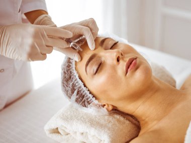 Güzellik uzmanı, genç esmer kadının yüzüne şırıngayla güzellik prosedürü uyguluyor. Kozmetik ilaç ve ameliyat, güzellik iğneleri.