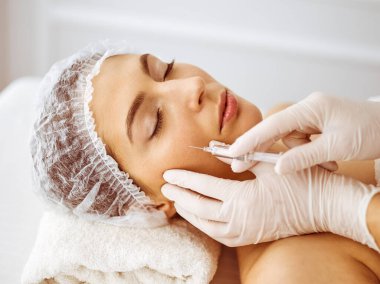 Güzellik uzmanı, genç esmer kadının yüzüne şırıngayla güzellik prosedürü uyguluyor. Kozmetik ilaç ve ameliyat, güzellik iğneleri.