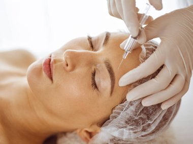 Güzellik uzmanı, genç esmer kadının yüzüne şırıngayla güzellik prosedürü uyguluyor. Kozmetik ilaç ve ameliyat, güzellik iğneleri.